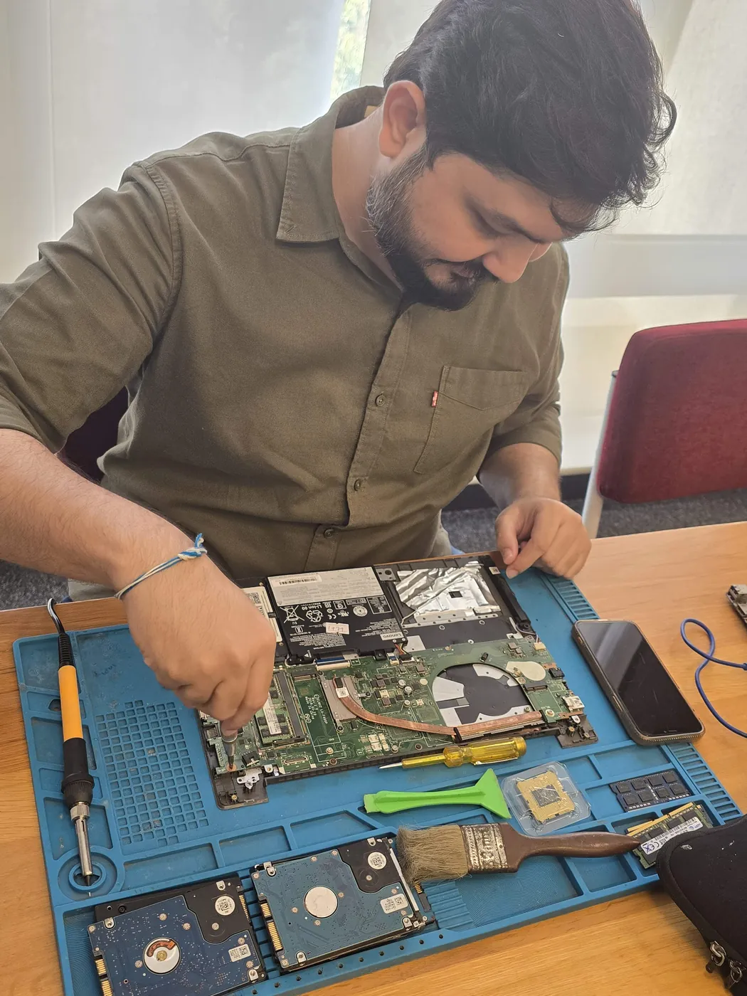 Technician working on an opened laptop with hard drives laid out on the repair mat