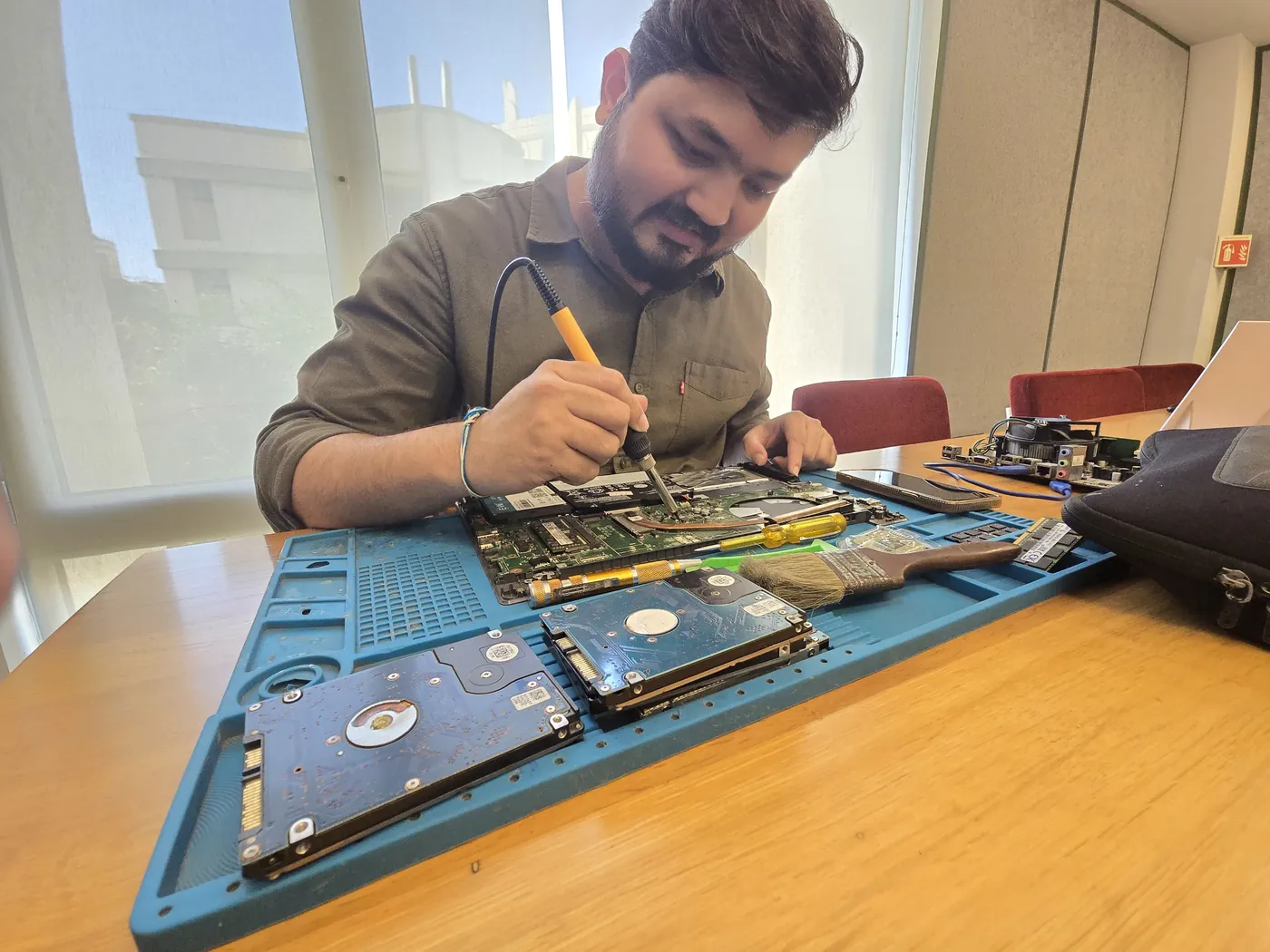 Technician soldering on a laptop board with two hard drives on the repair mat